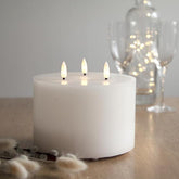 Fehér színű, viaszból készült, 3 darab meleg fehér fényű led lángú led gyertya fa asztalon, barkával az előtérben, háttérben borospohárral